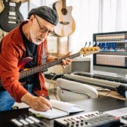 Developing A Bass Guitar Routine - Man holding bass guitar and taking notes while learning online